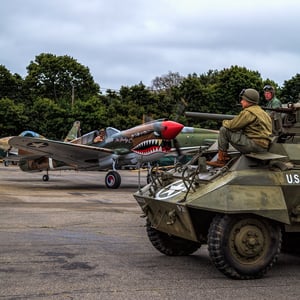 Man on assault vehicle in front of a jet with shark teeth on nose